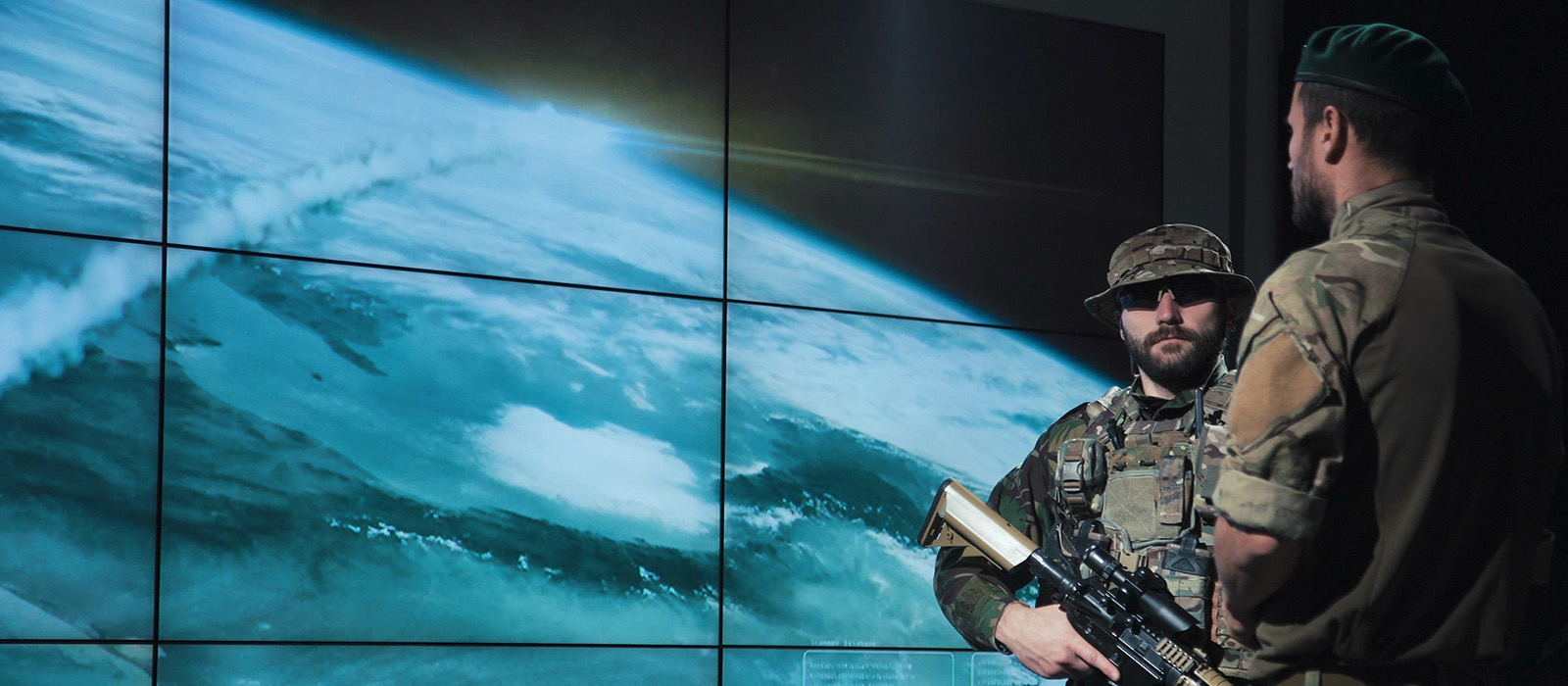 Two soldiers standing in front of a screen showing the world
