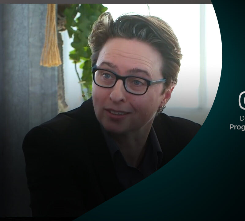 Bibi met een headsetmicrofoon tijdens een ESET-event, gefocust in gesprek. Rechts in beeld staat het ESET-logo met de slogan Digital Security – Progress. Protected.. De achtergrond is sfeervol met groene planten en natuurlijk licht.