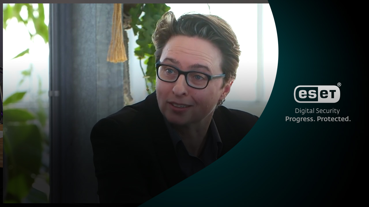 Bibi met een headsetmicrofoon tijdens een ESET-event, gefocust in gesprek. Rechts in beeld staat het ESET-logo met de slogan Digital Security – Progress. Protected.. De achtergrond is sfeervol met groene planten en natuurlijk licht.