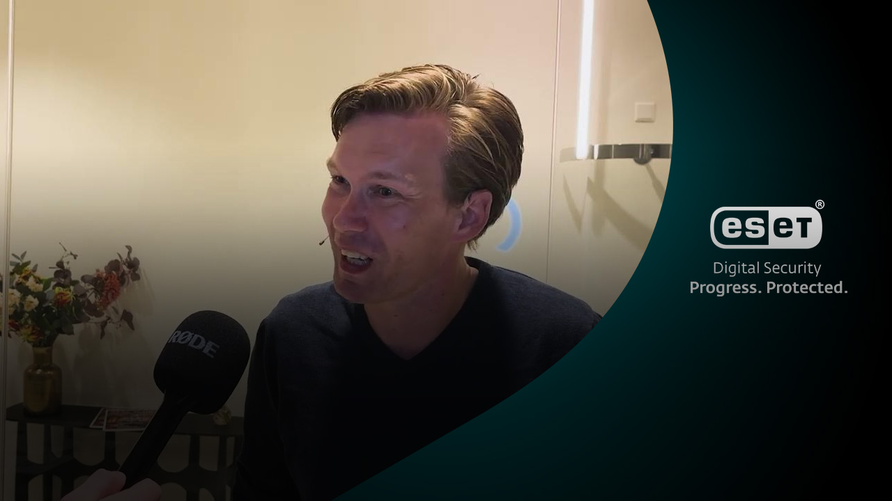 Geert Jan Hahn in gesprek met microfoon voor zich, met bloemen op de achtergrond.