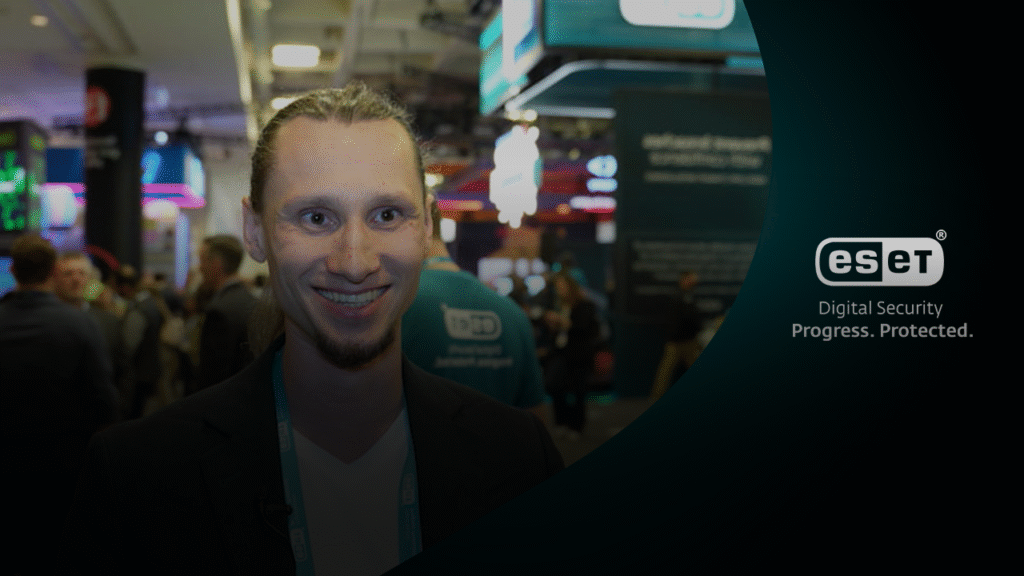 Juraj Janosik glimlacht voor de ESET-stand op RSA Conference 2025, omringd door bezoekers.